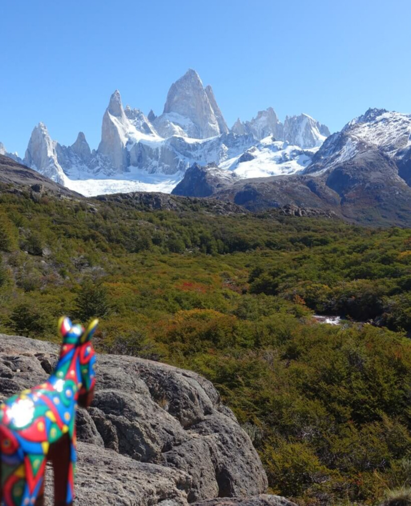 A little painted wooden donkey on a rock looking over a clear blue sky at the mountain Fitz Roy in Patagonia